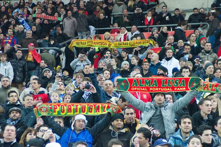 Portuguese national-team supporters fill a stadium stand, holding red-and-green scarves reading Portugal and Alma Lusa