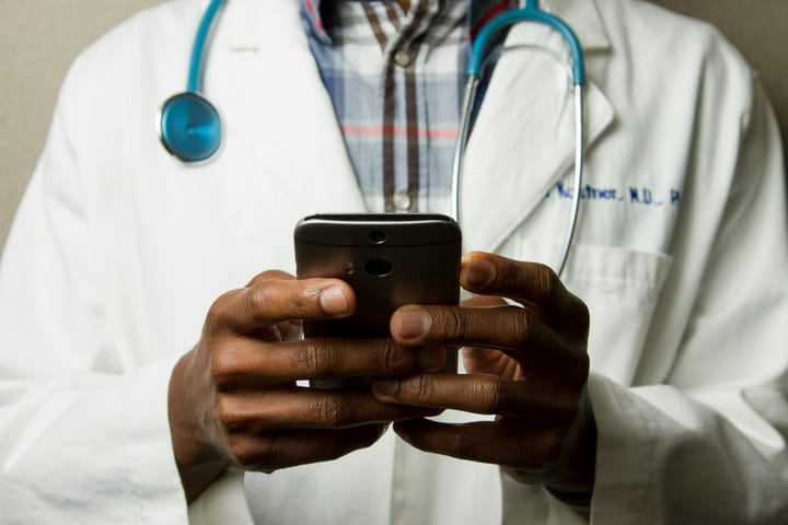 Health worker in a white coat with a stethoscope using a mobile phone