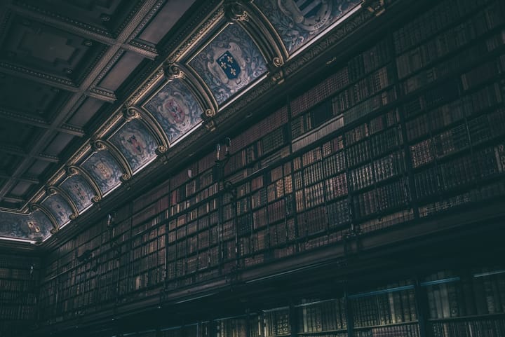 The interior of a grand historic library with tall shelves of antique leather-bound books beneath an ornate decorated ceiling