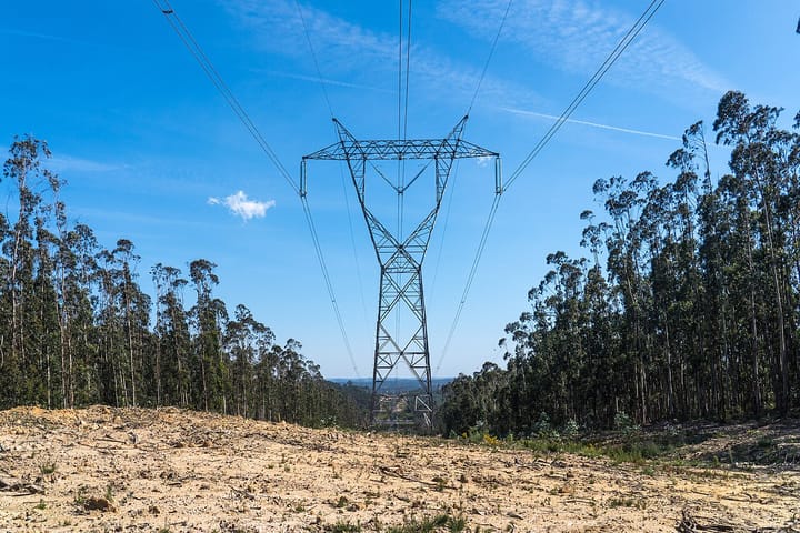 A high-voltage electricity transmission pylon and power lines crossing a Portuguese landscape near Rio Maior