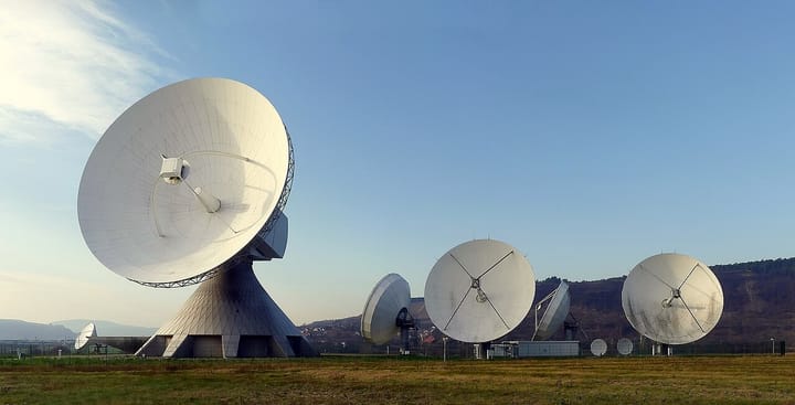 A row of large white parabolic satellite-dish antennas at a satellite earth station under a clear sky