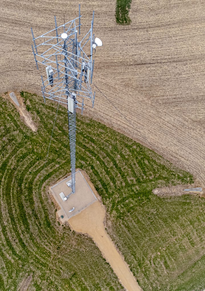 Aerial view of a steel mobile-phone telecommunications tower with antennas and microwave dishes in open countryside