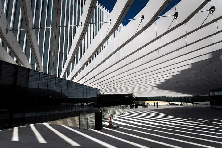 The white ribbed facade of EDP's Lisbon headquarters by Aires Mateus, its slatted canopy casting striped shadows across the riverfront plaza