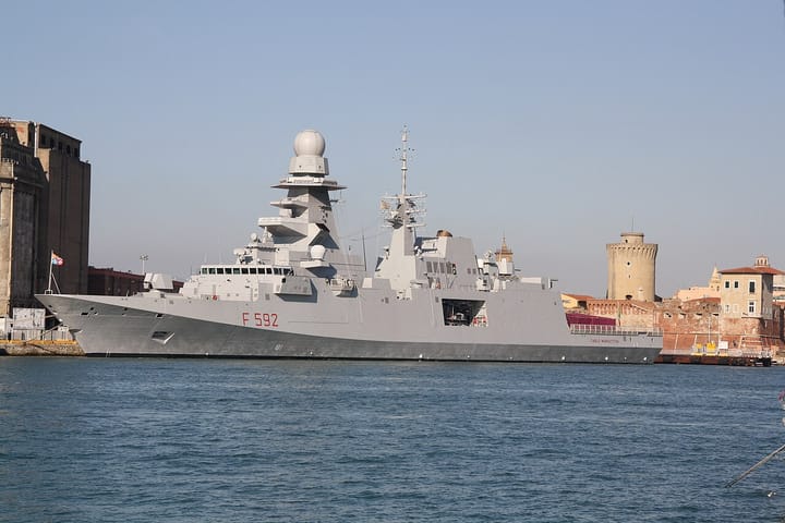 An Italian Navy FREMM multi-mission frigate, hull number F 592, moored in a harbour under a clear blue sky
