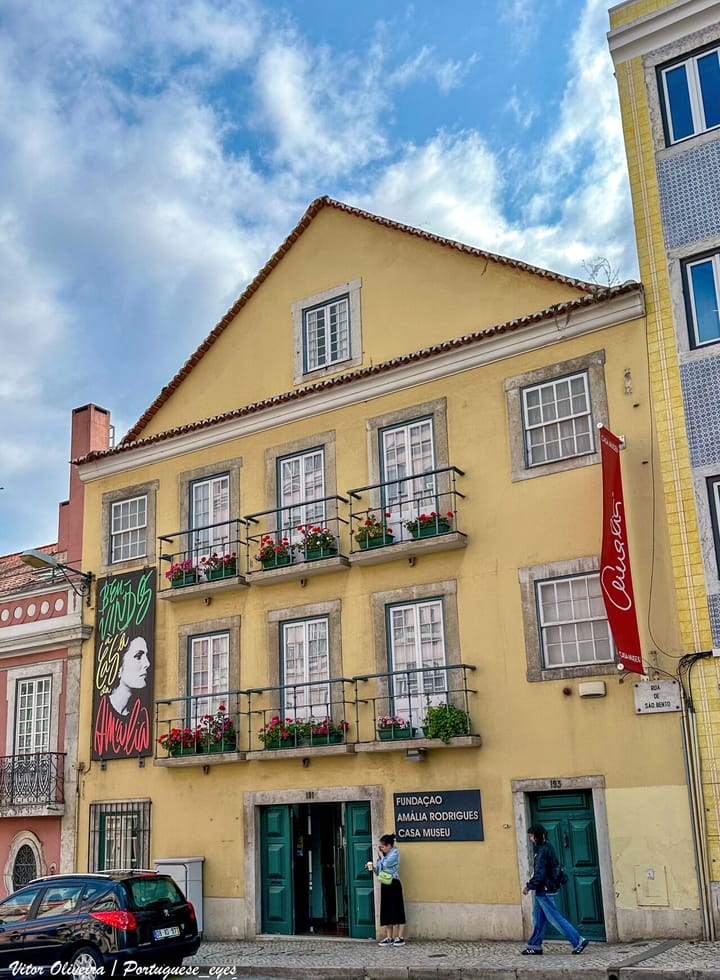 The yellow facade of the Casa-Museu Amalia Rodrigues on Rua de Sao Bento in Lisbon, with flower-filled balconies, red banners and a mural of the fado singer