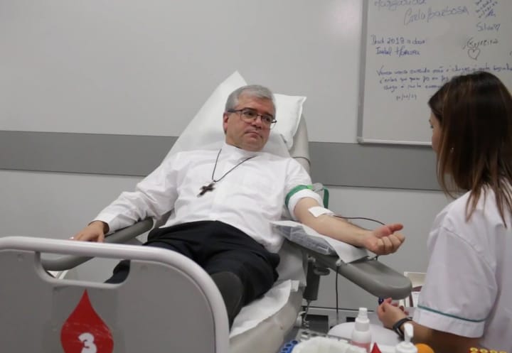 A man reclines in a donation chair with a needle taped into his arm while a health professional in a white coat attends to him at a blood collection service in Braga, Portugal