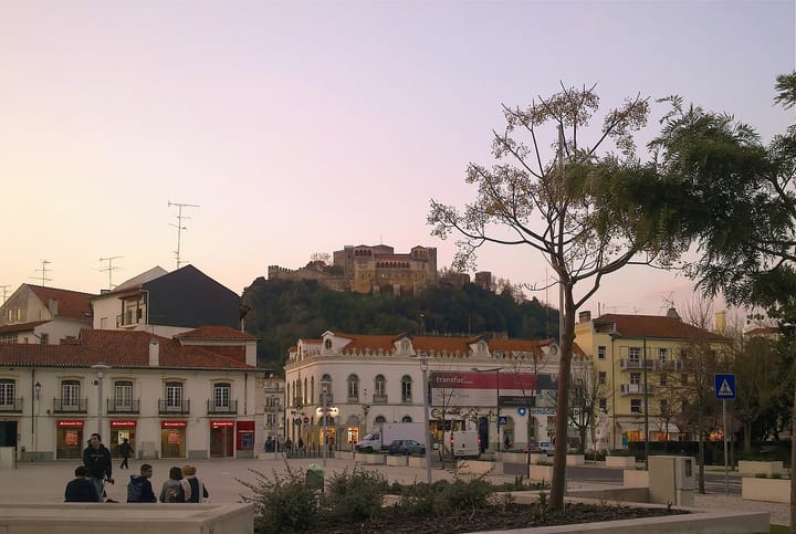 The medieval castle of Leiria rising on a wooded hill above the city's dusk-lit central square, in the district worst hit by Storm Kristin