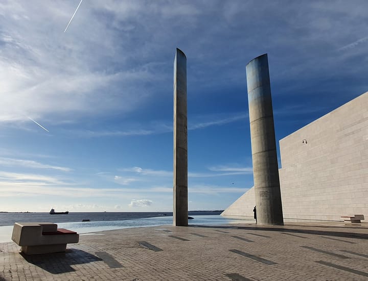 The two tall towers of the Champalimaud Centre for the Unknown, a Lisbon biomedical research campus, standing beside the Tagus estuary under a blue sky