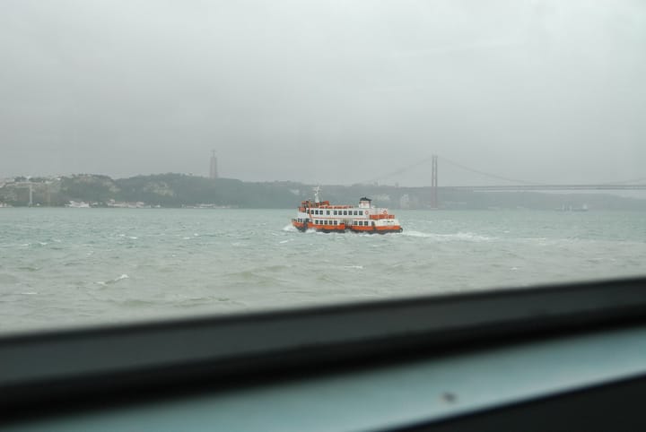 Orange and white Transtejo cacilheiro ferry crossing the Tagus river with the 25 de Abril bridge behind