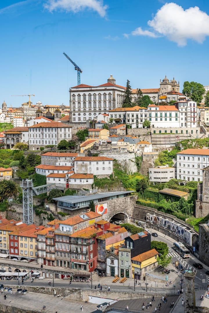Construction cranes rising over the historic riverfront buildings of Porto, Portugal, under a blue sky