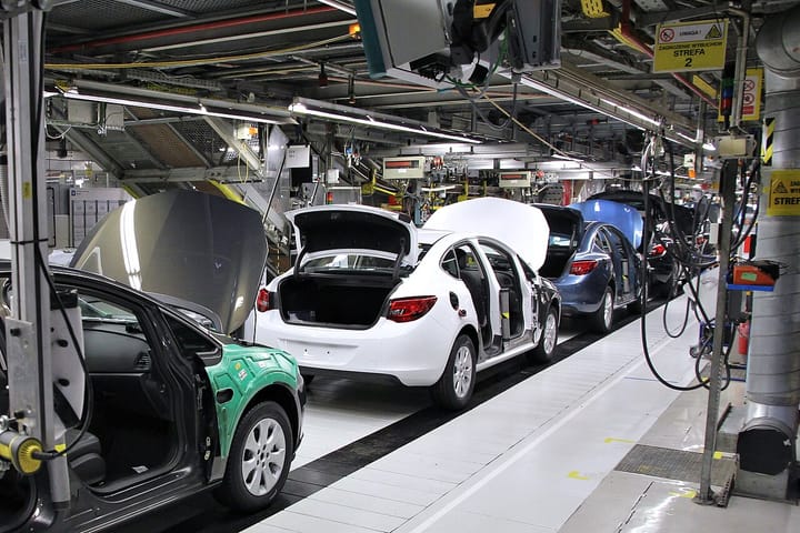 Cars moving along an automated assembly line in a car factory with overhead conveyor machinery