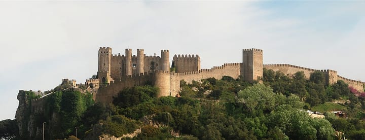 The medieval crenellated walls and towers of Obidos Castle on a green hillside in Portugal