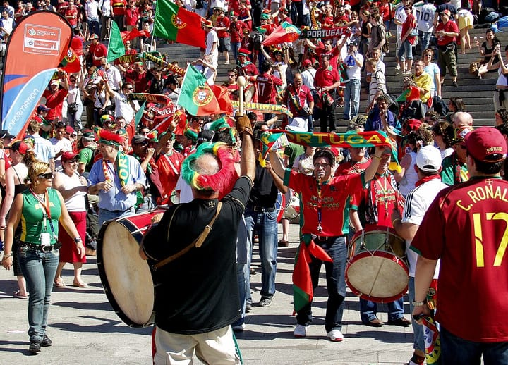 Portuguese national-team supporters in red and green shirts waving flags and beating drums at a match