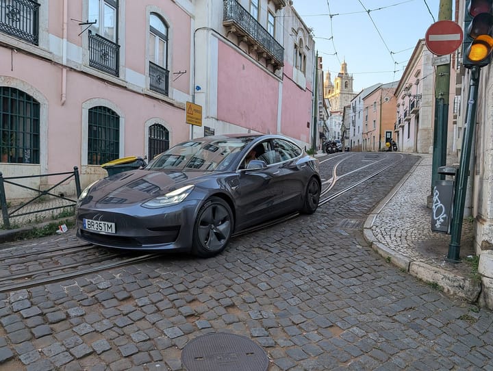 A Tesla Model 3 with Portuguese plates crossing tram tracks on a cobbled street in Lisbon