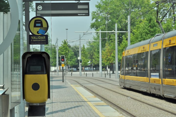 A yellow Metro do Porto light-rail tram waiting at a station platform in Porto, Portugal, beside an Andante ticket validator