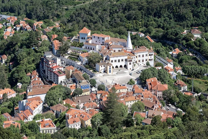 Aerial view of the historic centre of Sintra, Portugal, with the white National Palace and its twin conical chimneys surrounded by red-tiled roofs and forested hills