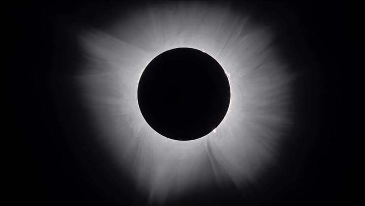 A total solar eclipse with the Sun's white corona streaming around the black disc of the Moon
