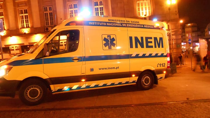 A yellow INEM ambulance of Portugal's National Institute of Medical Emergency responding at night on a street in Porto, blue lights flashing