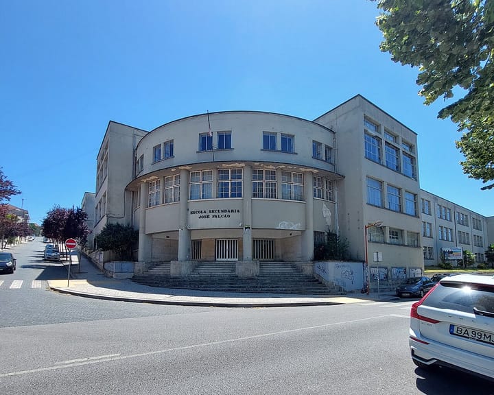 The curved Art Deco facade of the Escola Secundaria Jose Falcao in Coimbra, a Portuguese state secondary school, its name carved above the entrance under a clear blue summer sky