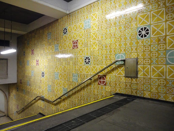 The interior of a Lisbon Metro station with its distinctive yellow patterned azulejo tiles and a stairway handrail