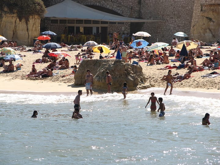Sunbathers under umbrellas and swimmers in the sea at a busy sandy cove beach in Lagos, on Portugal's Algarve coast