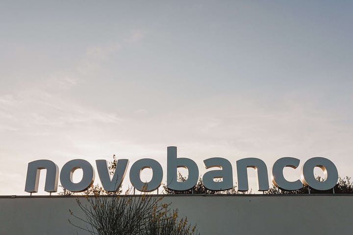 The illuminated novobanco logo mounted on the roofline of a bank building against a pale evening sky in Portugal