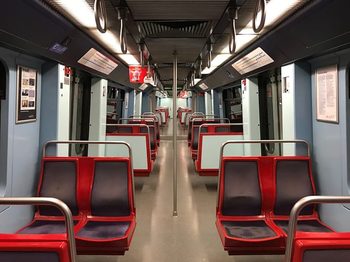 Interior of a Lisbon Metro train carriage with red seats and route maps on the walls