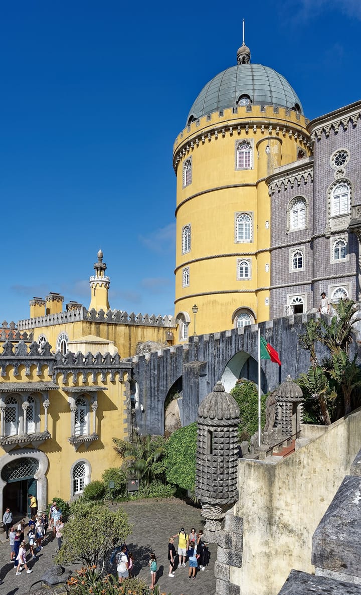 The yellow domed tower of the Palácio da Pena above Sintra, with visitors gathered on the terrace below and the Portuguese flag flying