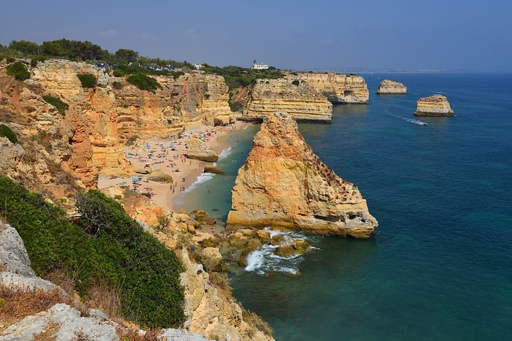 The cliff-backed cove of Praia da Marinha on Portugal's Algarve coast, golden limestone stacks and sunbathers on the sand beside turquoise Atlantic water