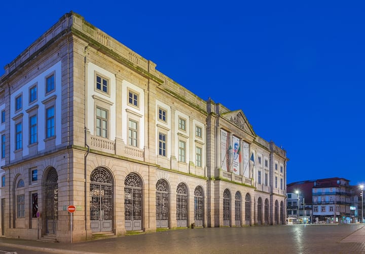 The neoclassical stone facade of the Rectory of the University of Porto lit at blue hour