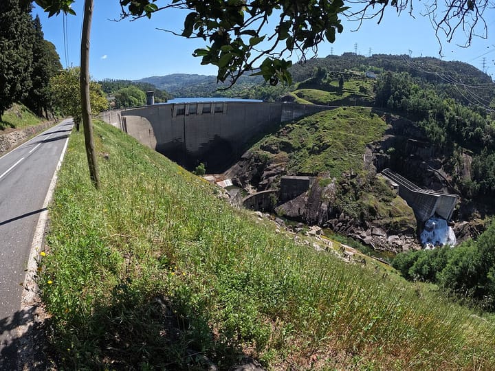 The Barragem da Caniçada dam and its reservoir in northern Portugal, a road running along the tree-lined hillside under a clear blue sky