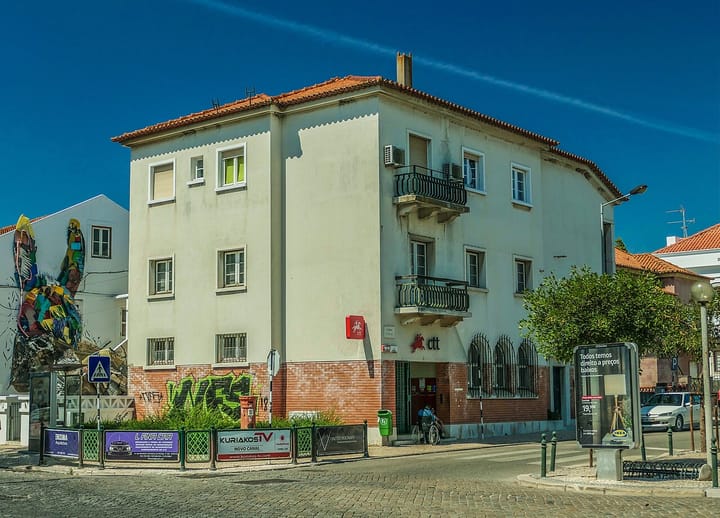 A Portuguese CTT post office building on a street corner in Montijo, its red-and-white ctt logo visible above the entrance under a clear blue sky