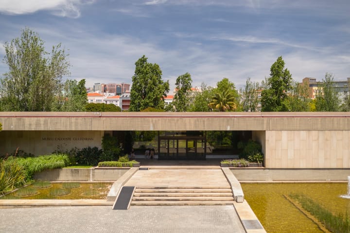 The low modernist entrance of the Calouste Gulbenkian Museum in Lisbon, its name carved in stone above a reflecting pool and garden