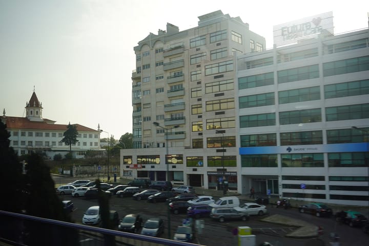 A row of cars parked along a Lisbon street in front of white apartment and office buildings, illustrating car dependence in the Lisbon Metropolitan Area