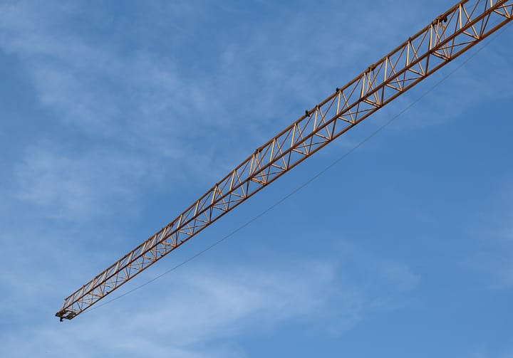The long steel jib of a construction tower crane angled across a clear blue sky over Lisbon, symbolising Portugal's public-works and construction sector