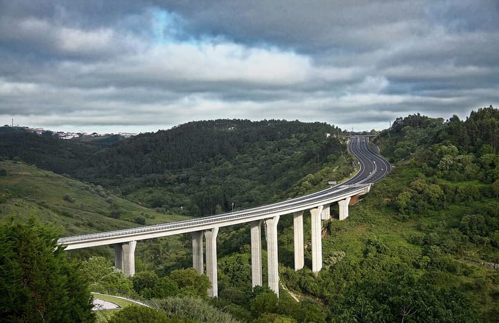 A Portuguese motorway viaduct curving through green wooded hills under a cloudy sky