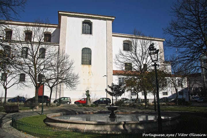 The tall whitewashed facade of the former Convento da Graca in Lisbon, with a stone fountain and garden square in the foreground