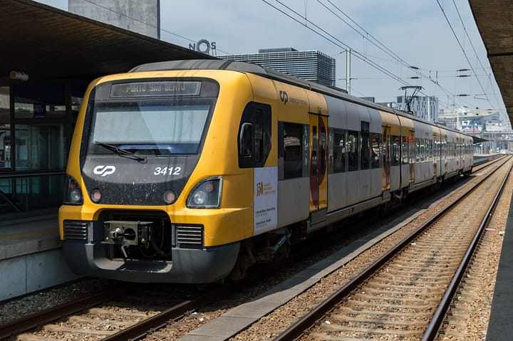 A yellow CP suburban train stopped at a Porto station platform under overhead electric lines