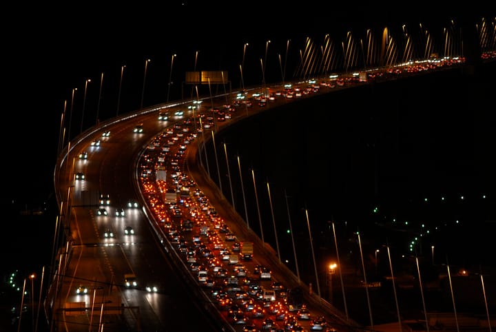 Heavy night rush-hour traffic streaming across the illuminated Vasco da Gama bridge over the Tagus in Lisbon, dense with red tail-lights and white headlights
