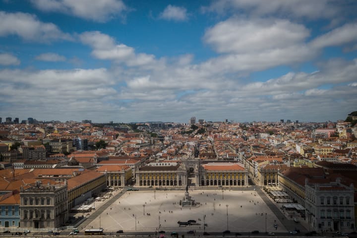 An elevated view over Lisbon's Praca do Comercio and terracotta rooftops beside the Tagus river