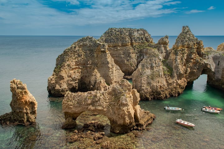The golden sandstone cliffs and sea stacks of Ponta da Piedade near Lagos in the Algarve, with clear turquoise water and small tour boats moored below a bright sky