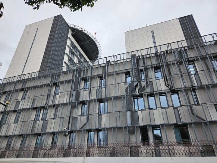 The modern grey facade of the Policia Judiciaria (Judicial Police) headquarters in Lisbon, with vertical metal louvres, dark glazing and perimeter security fencing