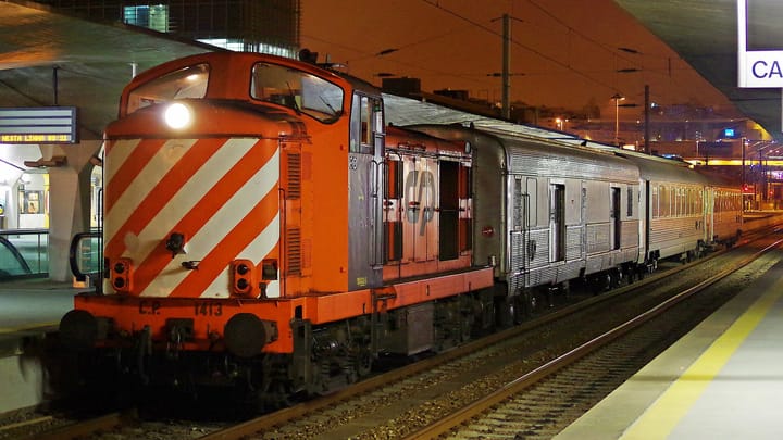 A CP Comboios de Portugal train with an orange locomotive at a Portuguese railway station platform