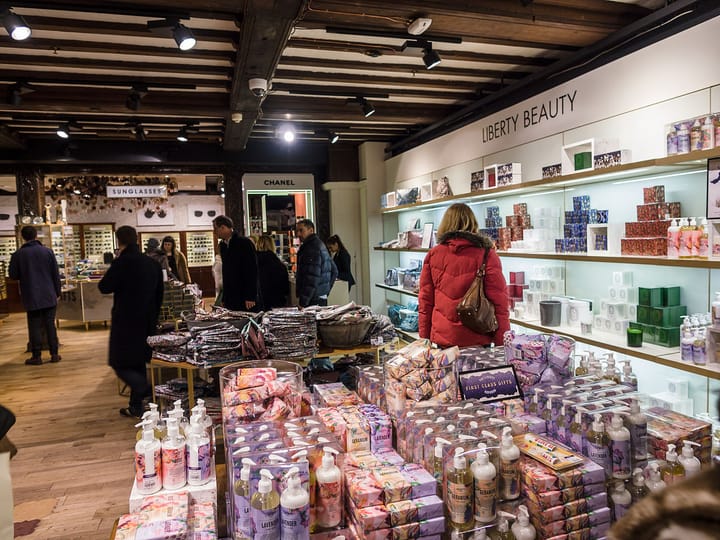 The interior of a beauty and perfumery store, with cosmetics and toiletries stacked on tables and shelves and a shopper browsing