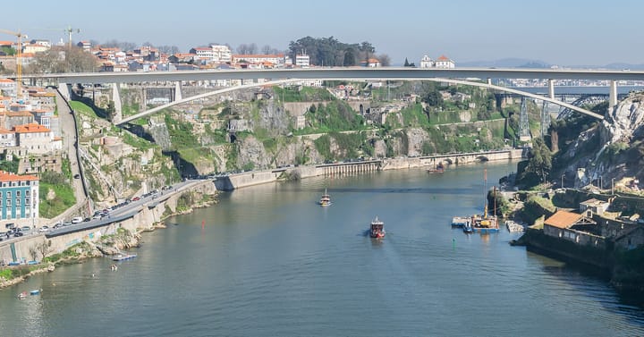 The Douro river gorge in Porto with the Ponte do Infante arch bridge, terraced houses on the steep banks and rabelo boats on the water