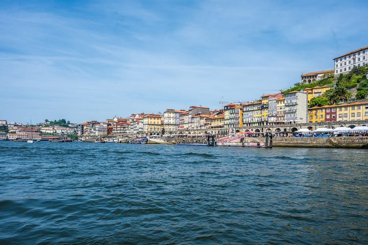 The colourful houses of Porto's Ribeira district lining the north bank of the Douro river under a bright summer sky, seen from the water