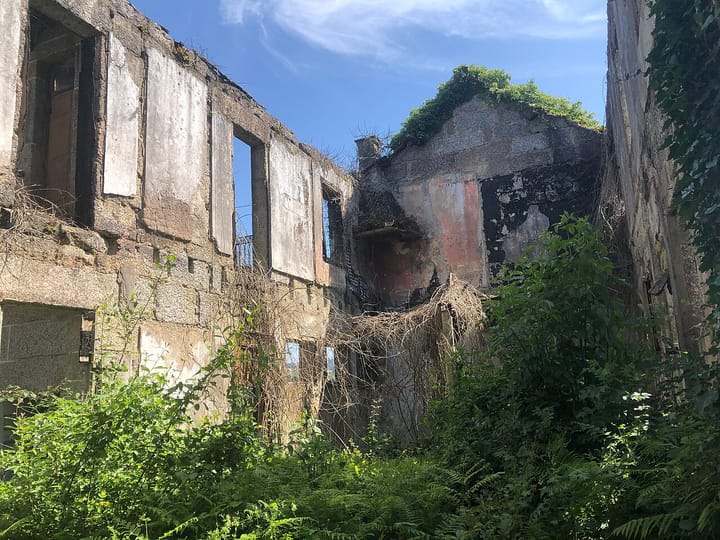 An abandoned, roofless stone house in Portugal overgrown with vegetation under a blue sky