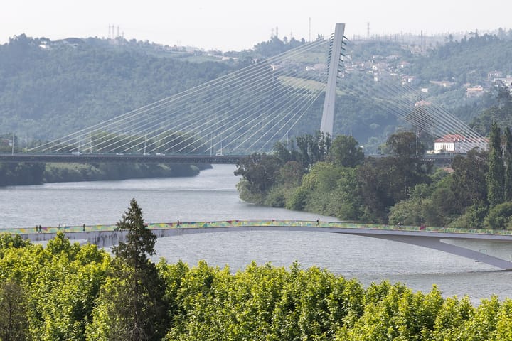 The Mondego river at Coimbra with a modern cable-stayed bridge and a curved footbridge crossing green riverbanks