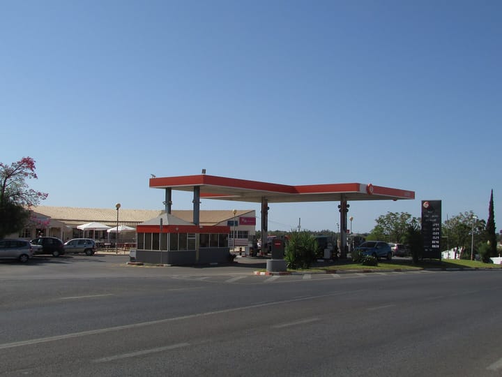 A Galp petrol station with its red-and-white canopy and a fuel-price board beside a road in the Algarve, Portugal, under a clear blue sky