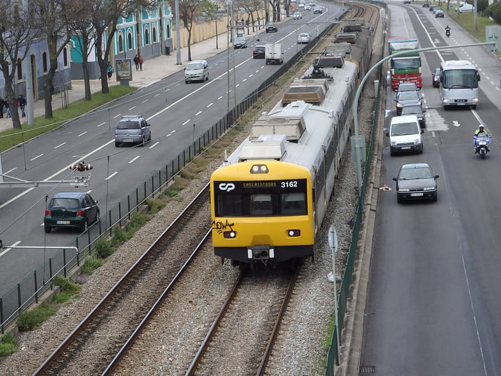 A yellow Comboios de Portugal (CP) suburban train on the Linha de Cascais running alongside a road in Belem, Lisbon